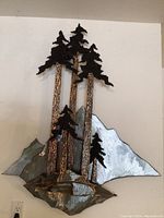 Full frontal view showing metal mountain and tree sculpture with dimensional layers and textures.