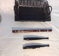 Overview of all items on a white cloth: black woven basket, carved wooden recorder, two black plastic recorders