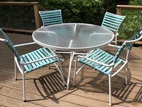 Full view of round glass top table and four aqua vinyl strapped chairs in white metal frames.