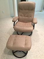 Front view of recliner chair and separate footstool showing light brown upholstery and black metal frames.