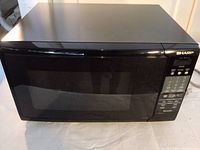 Front view of the Sharp black microwave oven with door closed showing control panel and exterior.