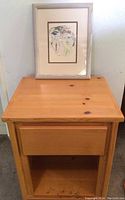 Nightstand top surface with framed artwork positioned on it, showing the wood grain and finish of the nightstand and the full framed art piece.