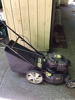 Side view of black Yard Machines lawn mower with grass collection bag attached, showing wheels and handle.