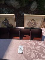 Photo showing wooden flat wall-mounted Hummel shelf with three compartments and two framed pictures behind it.