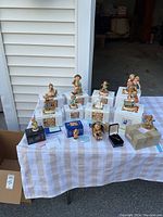 Wide shot of multiple Hummel figurines arranged on a table with original boxes, alongside a sterling silver necklace in a black box and a Goebel Collectors Club member coaster.