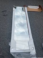 Two bypass sliding closet doors with mirrors, one showing cracks on mirror panel and both missing bottom track, resting outdoors on asphalt with packaging visible.