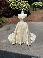 Front view of the vintage ivory wedding gown on a mannequin outside, showing the lace bodice, v-neckline, fitted waist, and full skirt.