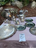 Photo showing entire set of silver plates, teapots, creamers, and large engraved serving tray with details of tarnish and design