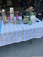 Long shot showing entire assortment of vases and candle holders on table with cloth in warehouse environment.