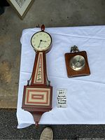 Photo showing the full wooden banjo clock with floral and geometric inlays alongside the vintage barometer on wood.