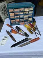 Photo showing plastic multi-drawer organizer with multiple compartments and various screwdrivers and knives laid out in front.