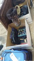 Overview photo showing brown UGG boots with fur lining, blue Crocs, multiple purses, all placed in a cardboard box near blue soft cooler bag.