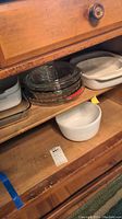 Wooden shelf with stacked clear glass Pyrex baking bowls and white ceramic CorningWare bowls.