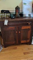 Front view of the vintage wooden cabinet showing two doors and one drawer, top surface with items on it.