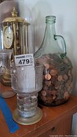 Image showing large glass jug filled with pennies, McDonald's Lord of the Rings goblet, and small glass jug together