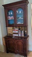 Full view of vintage two-piece wood china cabinet with glass-front upper section and solid lower doors showing contents and condition.