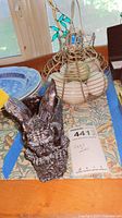 Resin dragon candle holder, wire chicken baskets containing stone eggs placed on a table with decorative cloth and blue plate in background.