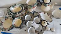 Full set of hand-painted ceramic dishware with cherry and leaf motif scattered on a white table, including plates, cups, tea pot, and shakers.