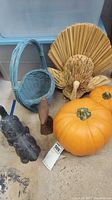 Photo showing a group of Thanksgiving decorative items including artificial pumpkins, cast iron dog figurine, wicker basket, wooden bird, and straw turkey.