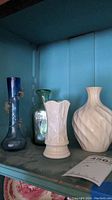Four vases displayed on a shelf: blue Lenox vase, green Belleek vase, white patterned vase, cream-colored patterned vase