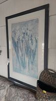 Framed floral wall art showing blue and white flowers with dark frame and matting.