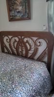 Wicker headboard shown attached to bed with patterned bedding, displaying full front view and placement.