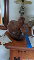 Front and side view of the wooden duck decoy on a wooden table with surrounding home decor.