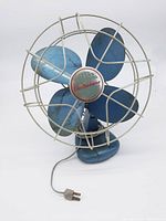 Front view of the blue Electrohome Long Life metal fan showing the four blue blades and protective silver metal cage with Electrohome logo center.