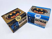 Front angle view of two unopened Batman card collection boxes, one gold and one blue, showing logos and card counts