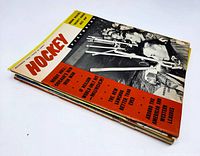 Stack of six vintage hockey magazines, the top one with black and white cover showing hockey equipment and players, with orange and black text