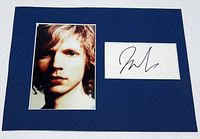 Front view of the matted color portrait photo of musician Beck alongside his autograph on white card, mounted on navy blue mat board.