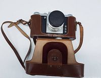 Top and front view of the Praktica FX camera fitted in a half leather case including strap.