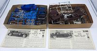Two open cardboard boxes containing plastic model kit parts in blue and brown colors alongside two instruction sheets for the 1931 Cadillac V-16 and 1935 Mercedes-Benz 500K models.