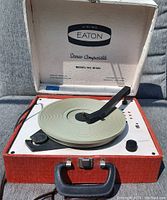 Photo showing open red suitcase-style portable record player with white lid interior. Label inside lid reads "Viking Eaton Stereo Compatible Model No. M 503." Cream-colored turntable, black tone arm, and control knobs visible.