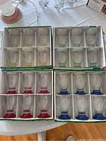 Photo of four boxes, each containing six glasses with colored bases (red, yellow, blue, green). Total 24 glasses.