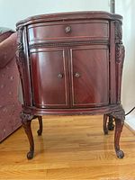 Front view of one dark wood side table showing drawer and two cabinet doors with carved legs.