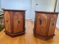 Front view of two hexagon-shaped end tables side by side, showcasing doors with round knobs and carved decorative trim.