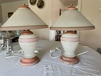 Pair of frosted glass table lamps with pink accent rings and matching frosted glass shades with pink edges placed on a table indoors.