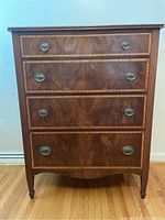 Front view of antique wooden chest of drawers showing four drawers with metal drop ring handles, visible wood grain and decorative inlay.
