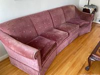 Full view of the curved high back 4-seat couch with pink floral upholstery showing shape, seat cushions, and armrest.