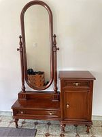 Front view of wood entrance organizer showing tall oval mirror with turned finials, wide lower drawer, and side cabinet with drawer and door.