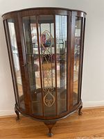 Front view of halfmoon wood curio cabinet with glass front, sides, mirror back and gold-tone decorative metal scrollwork on the door.