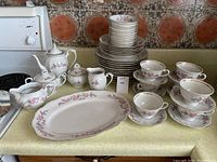 Full view of china set with multiple stacked plates, cups, saucers, teapot, creamer, sugar bowl and serving platter on kitchen counter.