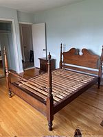 Full view of the maple wood four-poster bed frame set up in a bedroom showing headboard, footboard, side rails and wooden slat mattress support.