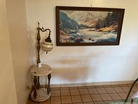 Photo showing the marble lamp with two round marble shelves and decorative curved lamp arm, placed against a wall beneath the landscape painting. Shows condition and size relative to wall and floor tiles.