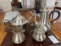 Four-piece silver plated tea and coffee set including coffee pot, teapot, sugar bowl, and creamer on hardwood floor.