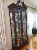 Front and side angle showing full cabinet with decorative top and glass doors