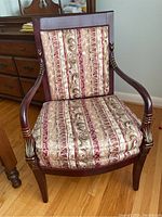 Front view of the upholstered side chair showing striped and scroll-patterned fabric on seat and back cushions and carved wood frame with gold accenting on arms