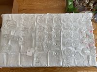 Top-down photo showing 35 various crystal glasses laid out on white cloth, including wine glasses, cocktail glasses and tumblers with etched patterns.
