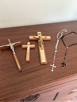 Three wooden crucifixes and two rosaries laid out on a wooden surface.